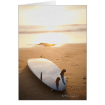 Planche de surf s'étendant sur la plage au coucher cartes de vœux
