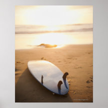 Planche de surf s'étendant sur la plage au coucher posters