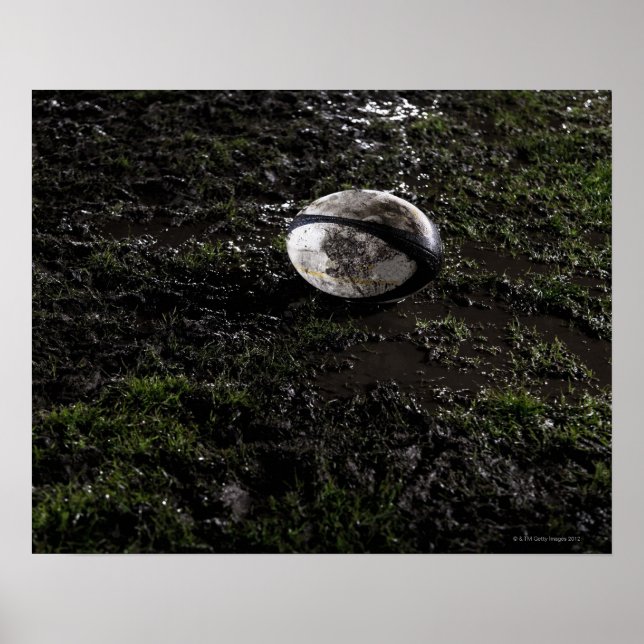 Affiches Muddy rugby ball sitting on a chewed up grass (Devant)