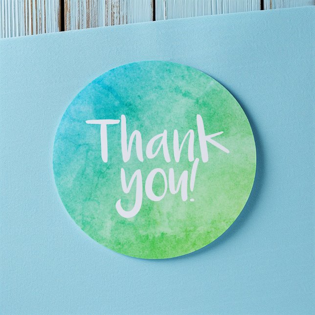 Autocollant vert clair aquarelle Merci (Round thank-you sticker with a blue and green watercolor gradient and handwritten-style white text)