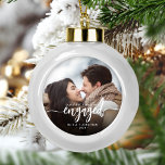 Boule En Céramique Premier Noël Engagé Photo personnalisée Script bla<br><div class="desc">Commémorez votre fiançailles avec ce magnifique ornement de gardien moderne. Le texte blanc dit "Notre premier Noël engagé", avec le mot "engagé" dans un élégant script de calligraphie avec des échasses décoratives avant et après. Remplacez l'exemple d'image par votre photo préférée, et ajoutez vos noms et l'année. Un filtre dégradé...</div>