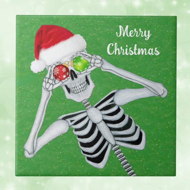 Carreau Sourire Noël Squelette Ornament Eyes Vert (Green Christmas decorative ceramic tile with Santa skeleton holding ornaments up to eyes.)