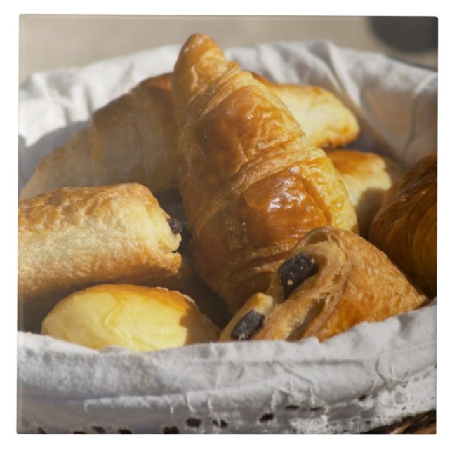 Carreau Un panier petit-déjeuner en osier avec croissants. (Devant)