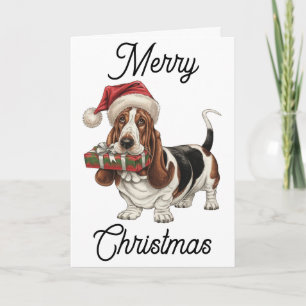 Carte Basset Hound avec un chapeau de Père Noël tenant u