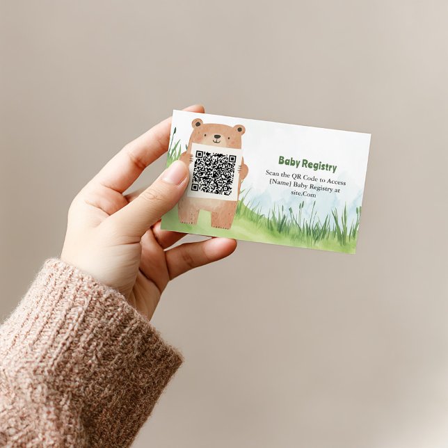 Carte d'enregistrement de code QR de l'ours adorab (Cute bear holding QR code for baby registry on grass background.)