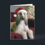 Carte La hache afghane de Noël sur un canapé en velours<br><div class="desc">Un beau chien de chien afghan avec de longs salons en fourrure soyeuse sur un canapé en velours rouge,  portant un chapeau de Père Noël festif. Le texte intérieur peut être modifié.</div>