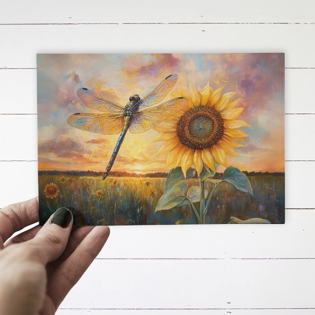 Carte Postale Libellule iridescente Soleil rustique (Postcard with a dragonfly and a sunflower being held up by a hand, over a white wood background.)