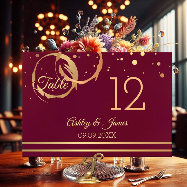 Carte rose Gold Marsala Wine Stains Table Numéro (Table number card featuring rose gold and gold wine stain rings with sparkling confetti on burgundy)