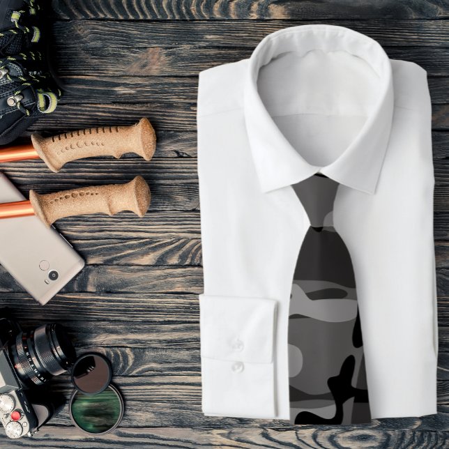 Col cravate camouflage gris et noir (A gray camo necktie is featured on a shirt and a assemblage of outdoors related accessories.)