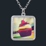 Collier Cupcake coloré avec cerise sur le dessus<br><div class="desc">Une photo estivale lumineuse d'un délicieux cupcake. Cette image a des nuages blancs et des montagnes dans l'arrière - plan. Le cupcake délicieux est contenu dans un emballage rose vif et rouge violet. Le cupcake lui-même est une combinaison de gâteau à la vanille et de glace au chocolat avec une...</div>