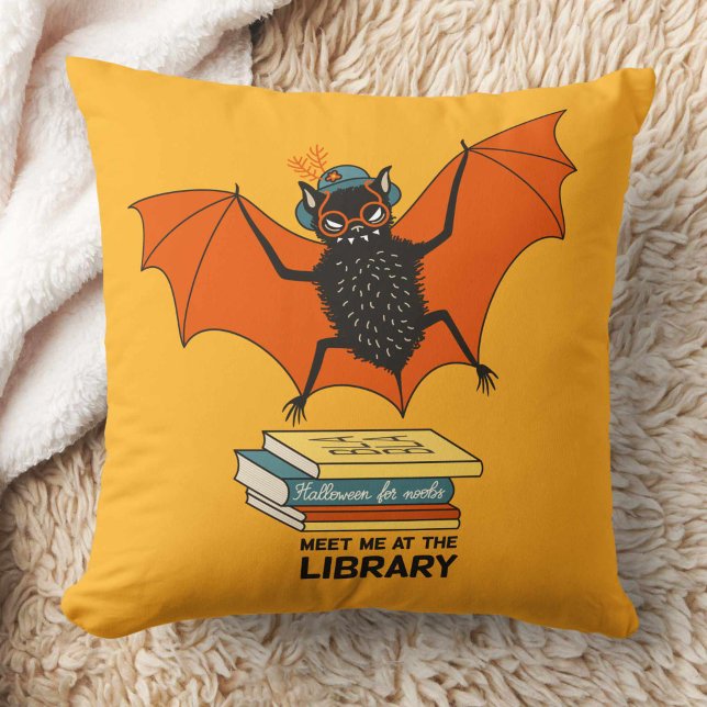 Coussin Chauve-souris lectrice | Bibliothécaire fantaisist (yellow pillow with a cute cartoon bat with eyeglasses and hat flying over some books)