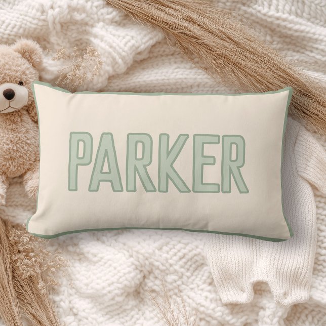 Coussin Rectangle Joli nom d'enfant personnalisé avec garniture faus (A cream pillow with "WILDER" in light sage green lettering lies on a cozy, soft-knit blanket)