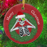 Décoration En Céramique Squelette en pin Noël Wreath Red Casquette Funny<br><div class="desc">Cet ornement en céramique suspendue a un drôle de squelette tenant des ornements avec des flocons de neige jusqu'à ses yeux en portant un chapeau de Père Noël rouge à l'intérieur d'une couronne d'épingle verte sur un arrière - plan rouge profond. Customisez votre texte à l'arrière avec le et le...</div>