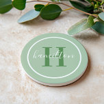 Dessous De Verre En Grès Élégant monogramme rond en vert sauge script<br><div class="desc">Un élégant dessous de verre en grès présentant une initiale serif verte feuillue et un nom de famille personnalisé en script, encadré par un cercle blanc sur un fond vert sauge doux. Les tons terreux et organiques apportent une chaleur apaisante et botanique à n'importe quel espace. Un beau cadeau personnalisé...</div>