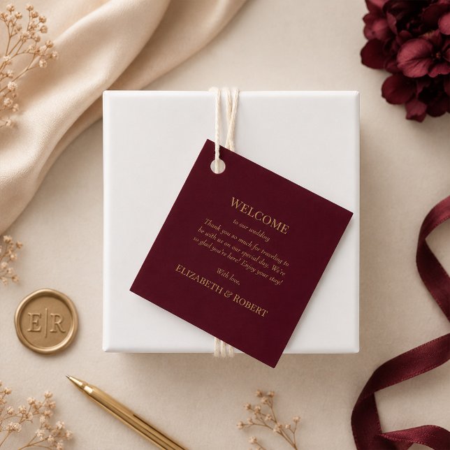 Étiquette de bienvenue de mariage floral Bourgogne (Modern Burgundy Floral Wedding Welcome Tag on a beige table with gold and burgundy wedding decor)