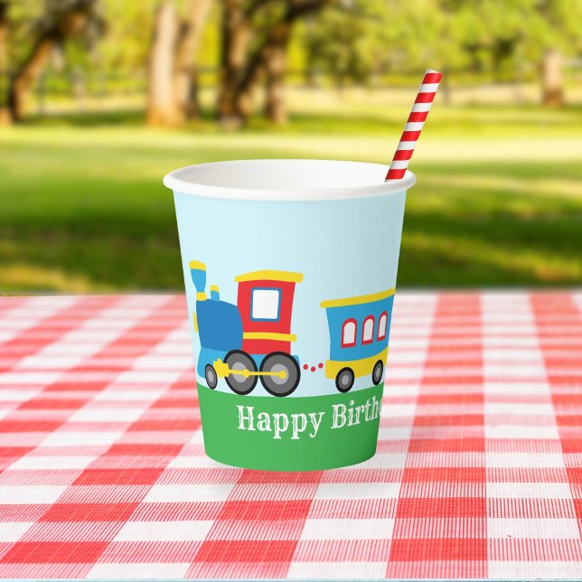 Gobelets En Papier Fête d'anniversaire Train Mignon (A paper cup decorated with a cute cartoon train sits on a picnic table in a park.)
