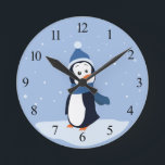 Horloge Ronde Pingouin (avec des nombres)<br><div class="desc">Un pingouin utilisant un casquette et une écharpe bleus se tient dans la neige et observe les flocons de neige tomber. Cette conception est disponible sur les produits multiples comprenant des chemises, des tasses, des coussins, et plus ! Elle peut être customisée ou personnalisée en ajoutant votre propre texte ou...</div>