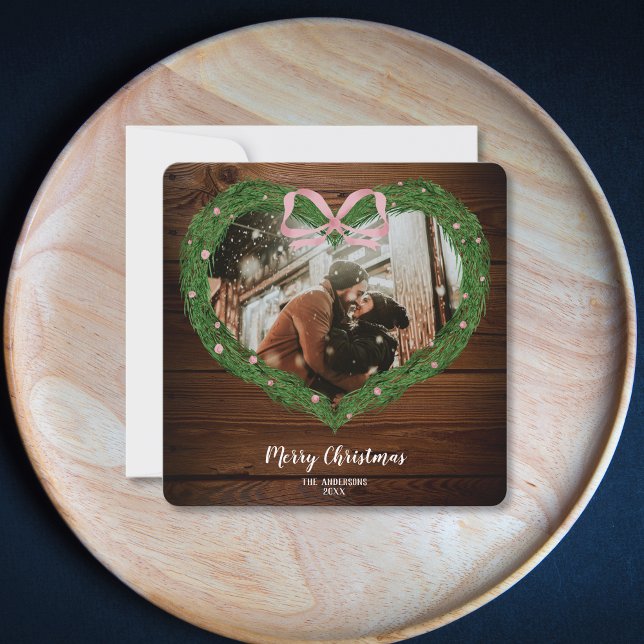 Invitation Ferme rustique Joyeux Noël Coeur Wreath Photo (heart shaped christmas wreath with a pink bow on the wood background)