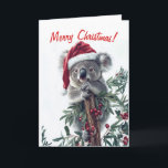 Koala dans une carte de Noël de chapeau de Père No<br><div class="desc">La carte de Noël comporte un koala mignon portant un chapeau de Père Noël et accroché à une branche avec de grandes baies rouges. Customisez le message et le message à l'intérieur de la carte à votre goût.</div>