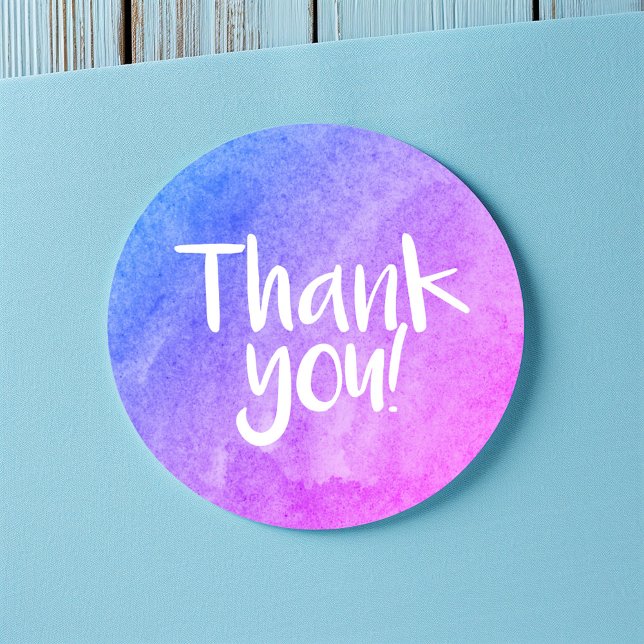 Merci autocollant brillant aquarelle (Round thank-you sticker with a blue and purple watercolor gradient and handwritten-style white text.)