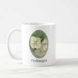 Mug Floral<br><div class="desc">Cette tasse est agrémentée de chaque côté d'oeuvres aux couleurs pastel douces picturant trois fleurs crémeuses d'hydrangée blanche en feuilles de chêne avec des bourgeons accentués en vert.</div>