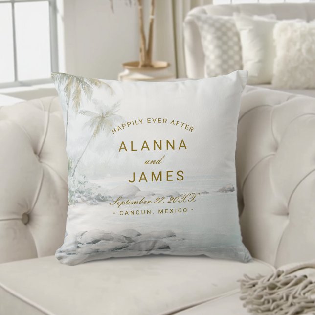 Oreiller de mariage de plage à l'aquarelle tropica (Beach-themed wedding pillow with “Alanna and James” and date text on a cream tufted sofa.)