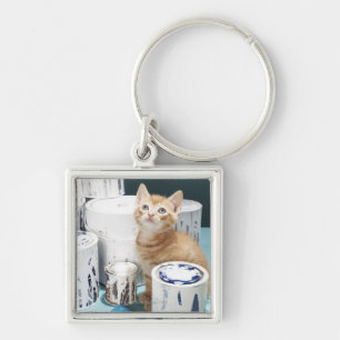 Porte-clés Chaton se reposant parmi des bidons de peinture
