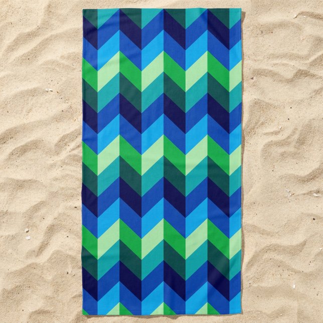 Serviette de plage à chevrons dégradés bleu-vert (Blue Green Ombre Chevrons Beach Towel lying in the sand.)