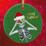 Silencieux Noël Squelette Casquette Ornements vert<br><div class="desc">Cet ornement en céramique suspendue a un squelette sot tenant des ornements rouges et verts à ses yeux tout en souriant et portant une fourrure de casquette du Père Noël rouge taillé sur un arrière - plan vert avec des taches de glitterie en faux or. Joyeux texte de Noël en...</div>