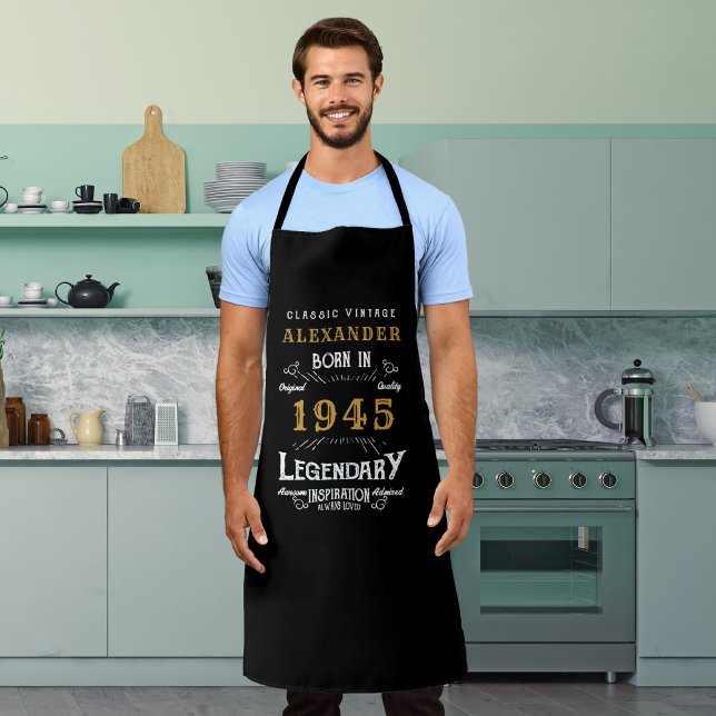 Tablier 80e anniversaire personnalisé Né en 1945 Noir Vint (Personalized 80th birthday legendary black and gold apron worn by a man in the kitchen)