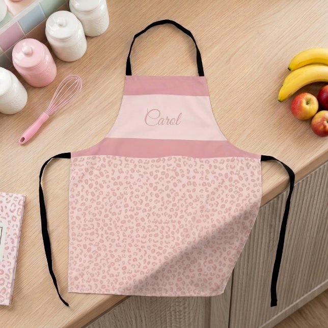 Tablier Imprimé léopard rose avec bande de nom guépard ray (Pink leopard print pattern personalized apron on a feminine pastel-decorated kitchen counter.)