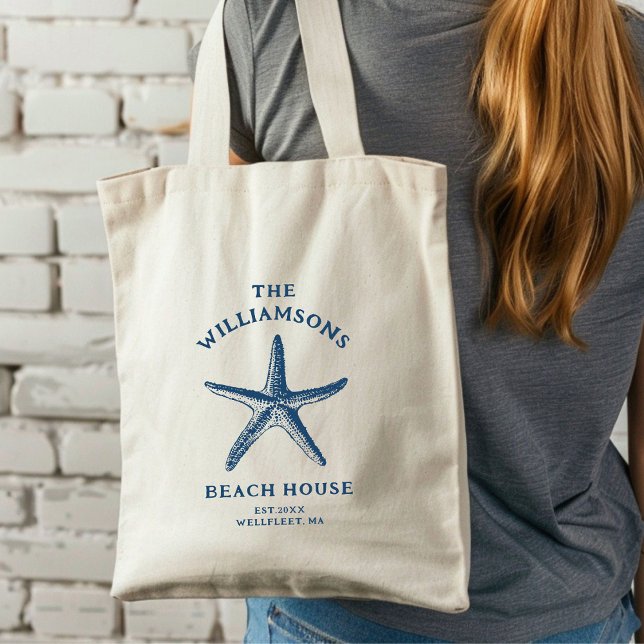Tote Bag Maison de plage de Starfish Côte Bleue Personnalis (A woman with long hair carries a cream tote bag featuring a blue starfish design.)