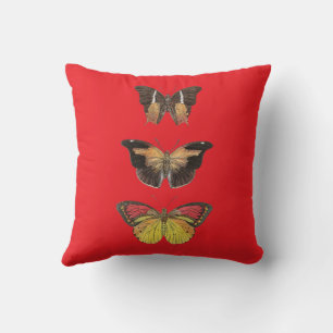 Trois papillons rouges et dorés sur un oreiller ro