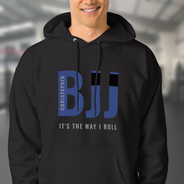 Veste À Capuche BJJ Brazil Jiu Jitsu Ajouter Nom Ceinture bleue (Blue Belt BJJ black hoodie worn by a male model in a gym.  )